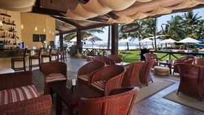 Un área de bar al aire libre con mobiliario de mimbre, una barra con botellas y vistas a la playa.