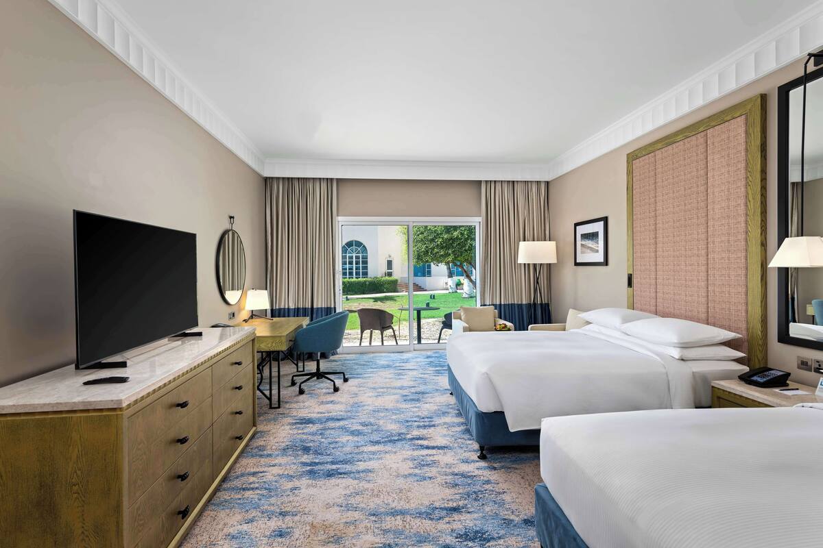 Habitación de hotel con dos camas, televisión, escritorio y vistas al exterior.