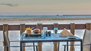 Mesa servida con una hamburguesa, ensalada y bebidas, con vista a la playa.