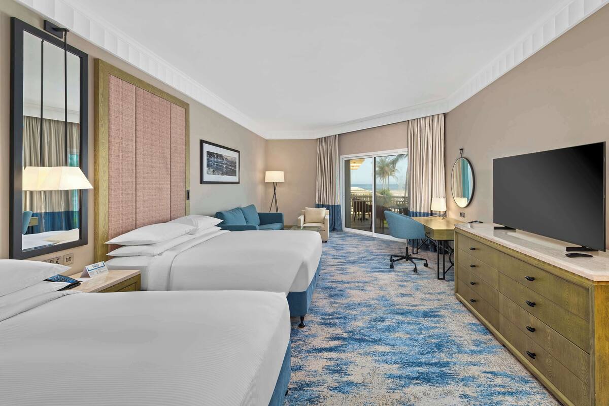 Habitación de hotel con dos camas, un escritorio, televisión y vistas al exterior.