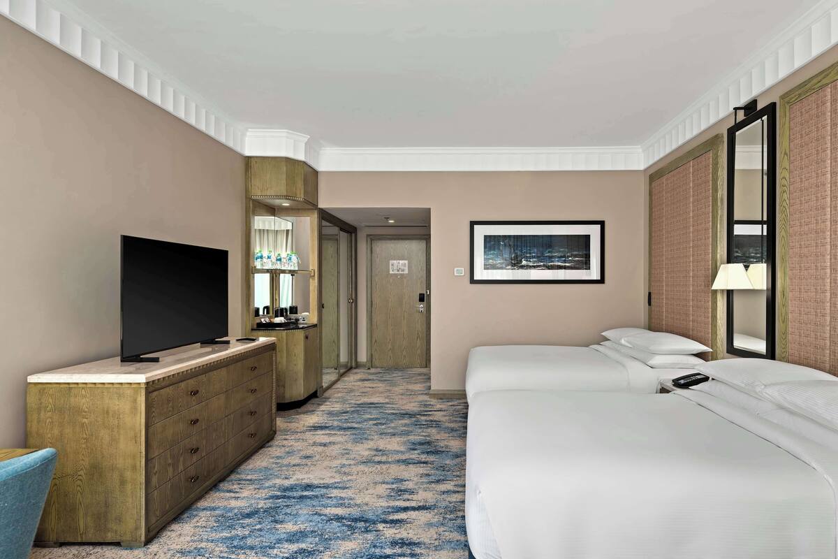 Habitación de hotel con una cama grande, un televisor en una cómoda de madera, un escritorio con lámpara y un cuadro en la pared.
