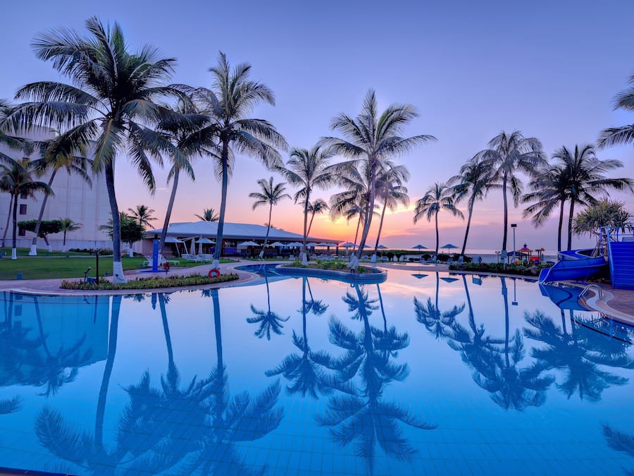 A swimming pool with palm trees and a building in the background.