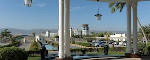 A hotel with a covered outdoor area featuring white columns, a glass balustrade, and a view of the surrounding landscape including mountains and buildings. - Hilton Salalah Resort (Salalah)