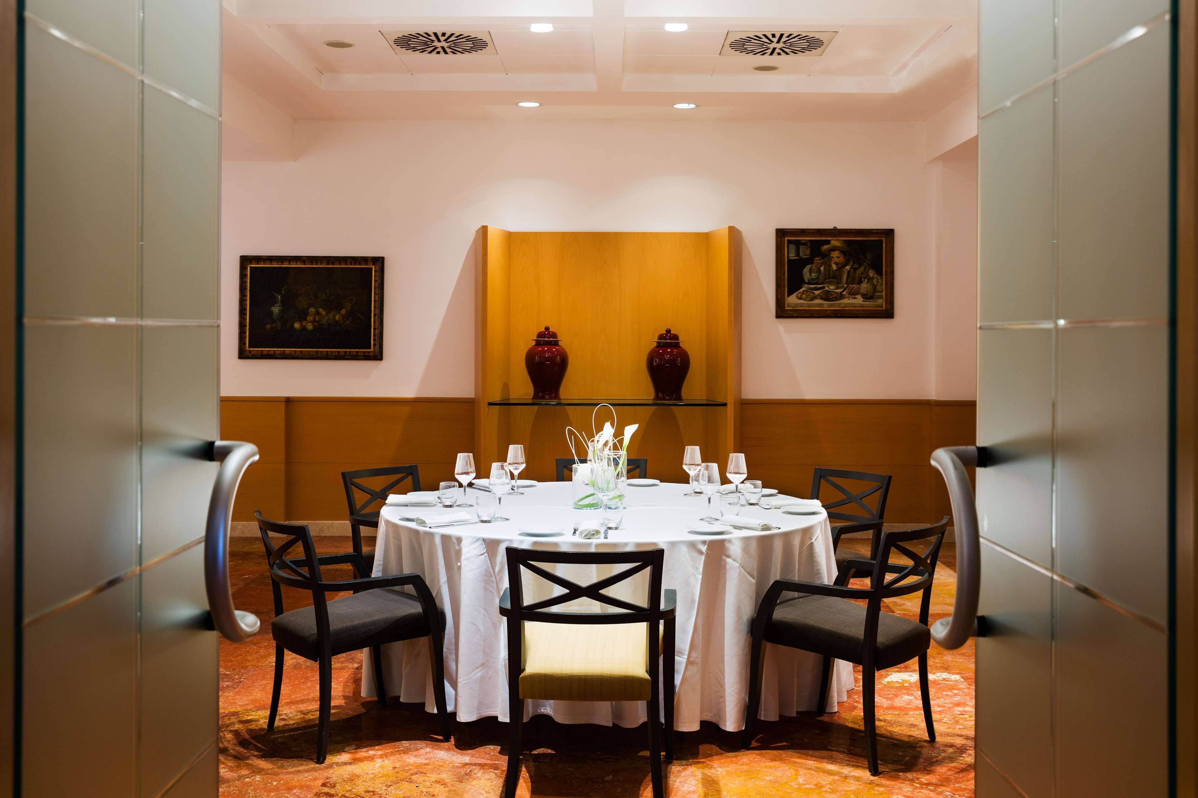 Una mesa redonda de comedor con mantel blanco, rodeada de sillas negras, en una habitación con un pared de acento amarillo y obras de arte enmarcadas.