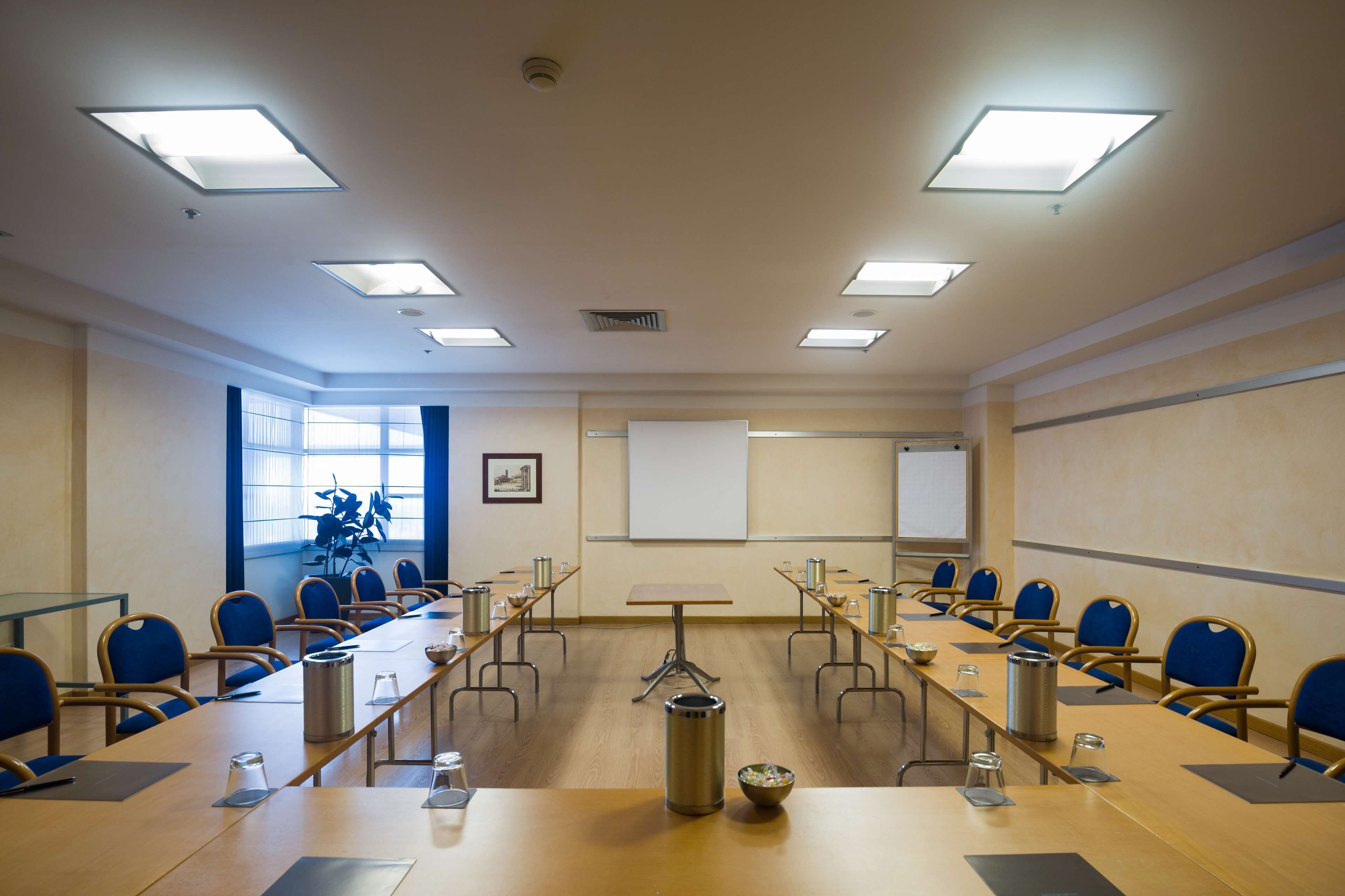 Una sala conferenze con un lungo tavolo, sedie, uno schermo per proiettore e una lavagna.