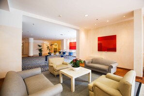 Relax in our spacious lobby, featuring a central seating area with sofas and a coffee table, surrounded by artwork and lush greenery.