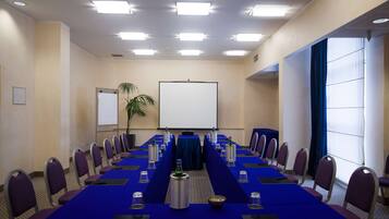 A conference room with a long table, chairs, a projector screen, and a plant.