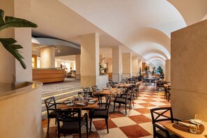 A spacious hotel lobby with a checkered floor, multiple dining tables, and a central reception area.