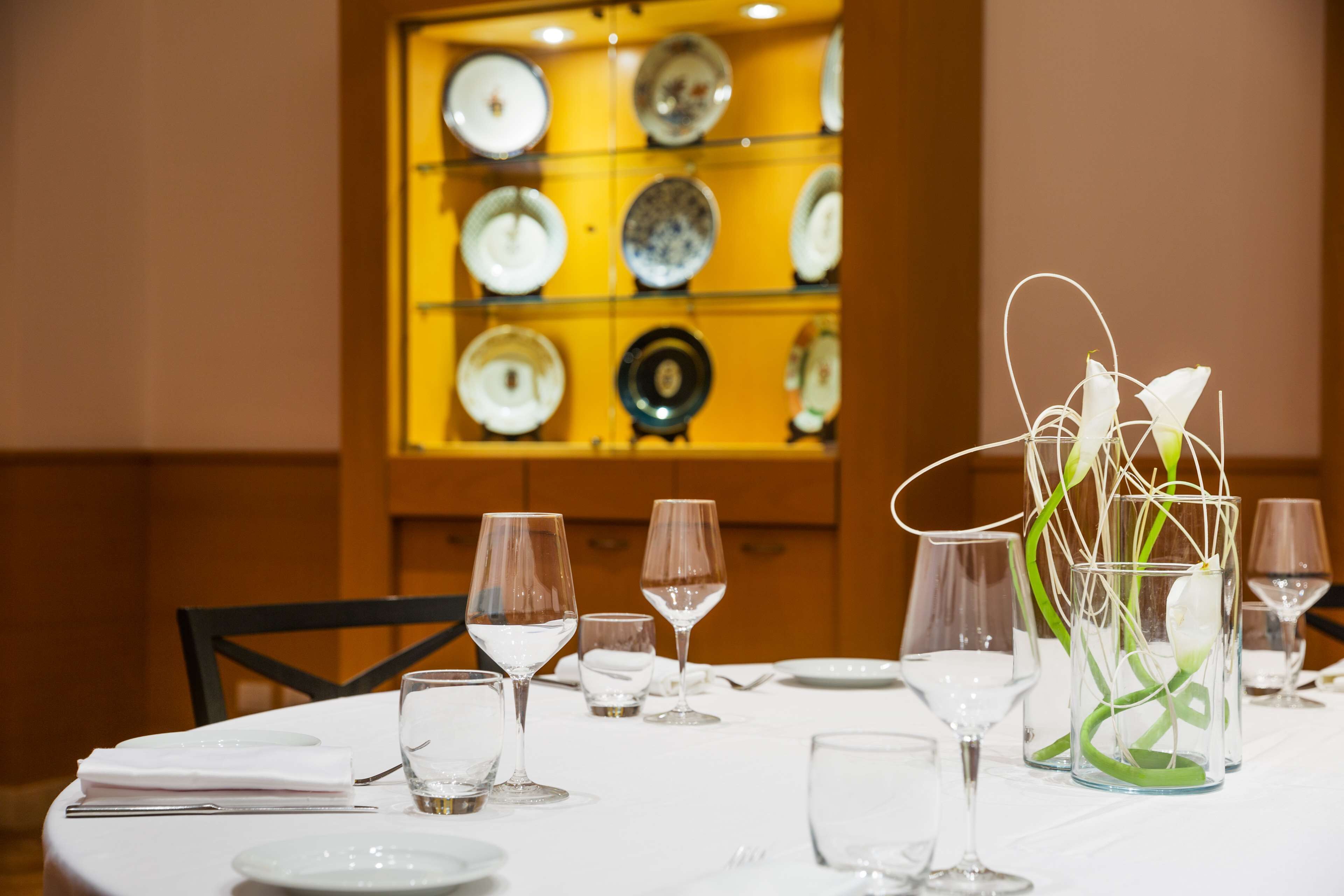 A dining table set with wine glasses and plates, with a decorative vase in the center.