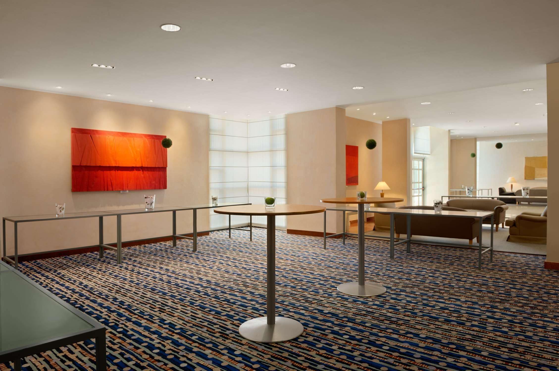 Un'accogliente hall d'hotel moderna, con tappeto a motivi geometrici, tavoli rotondi e un'area relax con divani.