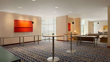 Un'accogliente hall d'hotel moderna, con tappeto a motivi geometrici, tavoli rotondi e un'area relax con divani.