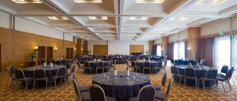 Une grande salle de conférence dotée de plusieurs tables rondes et de chaises, ainsi que de plaques nominatives et de bouteilles d’eau.