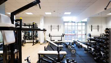 Un gimnasio con equipo de levantamiento de pesas, bancos y mancuernas.