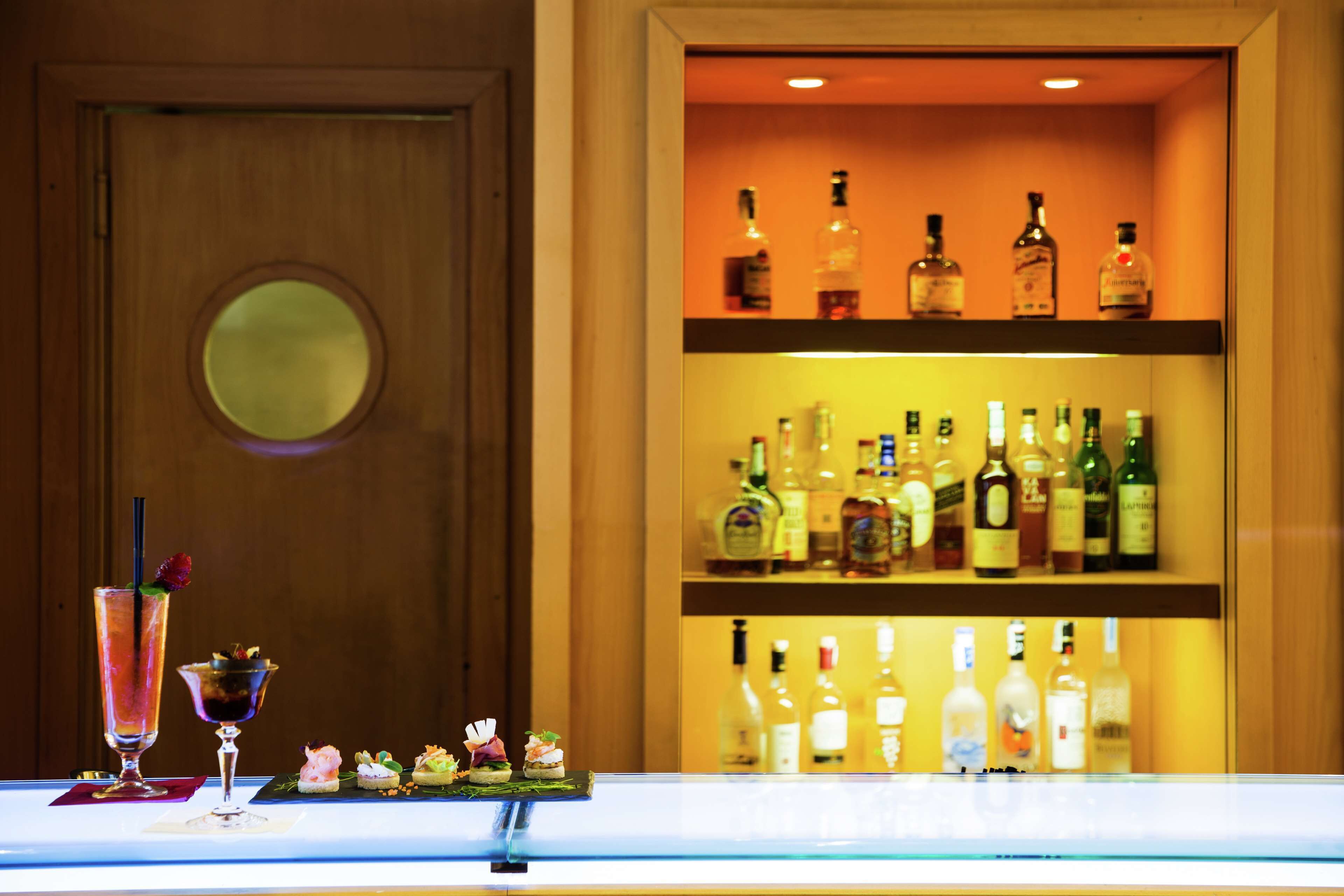 A bar area with shelves of liquor bottles and a selection of drinks and appetizers.