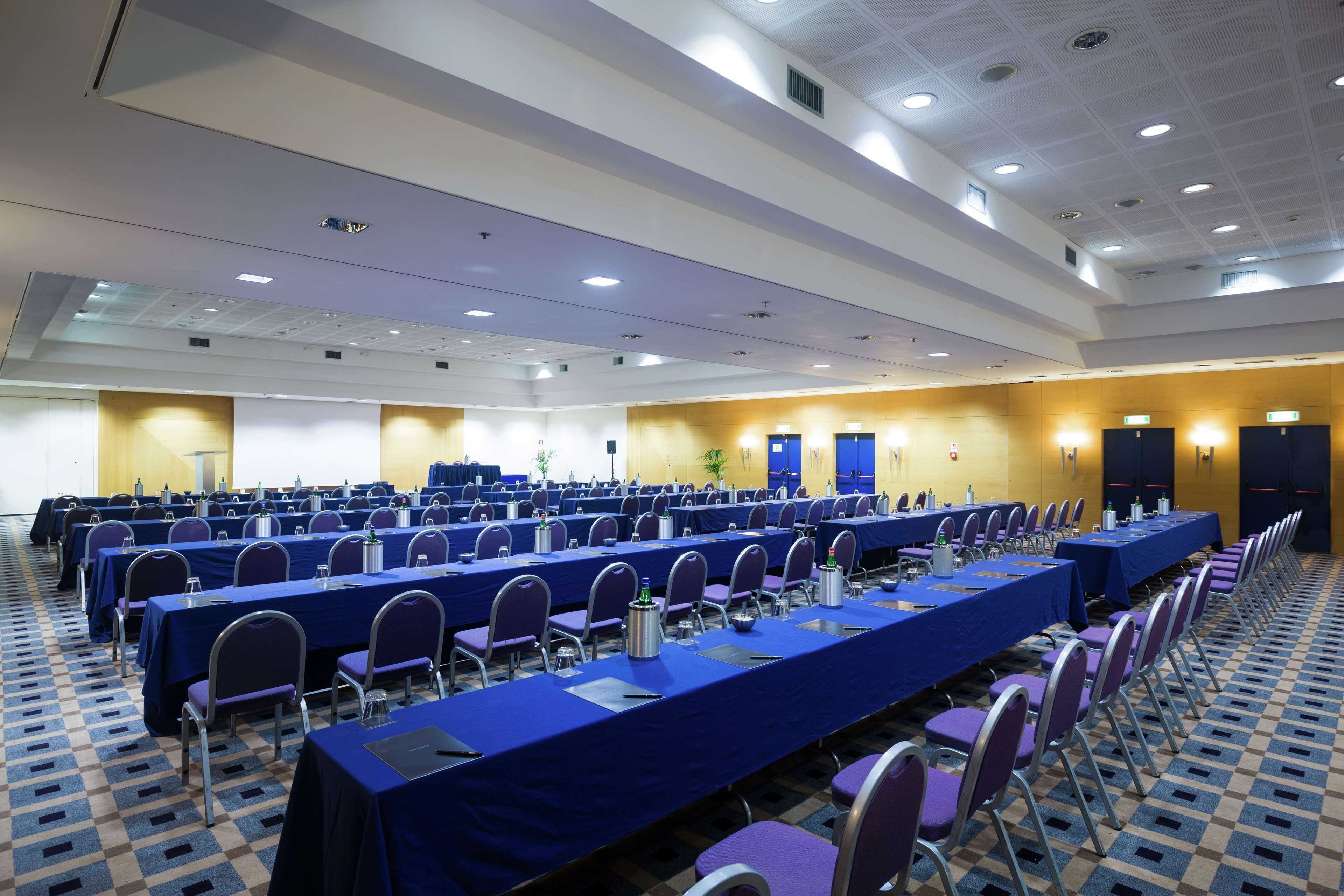 A conference room with rows of tables and chairs, equipped with water bottles and nameplates.