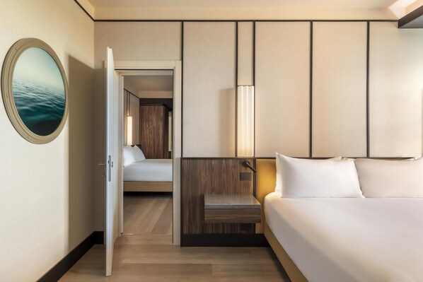 Habitación de hotel con una cama, una mesita de noche, un espejo y vistas al suelo de madera y otra habitación.