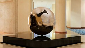 A modern sculpture in a lobby with a glass floor, beige walls, and a sign for a fitness center.