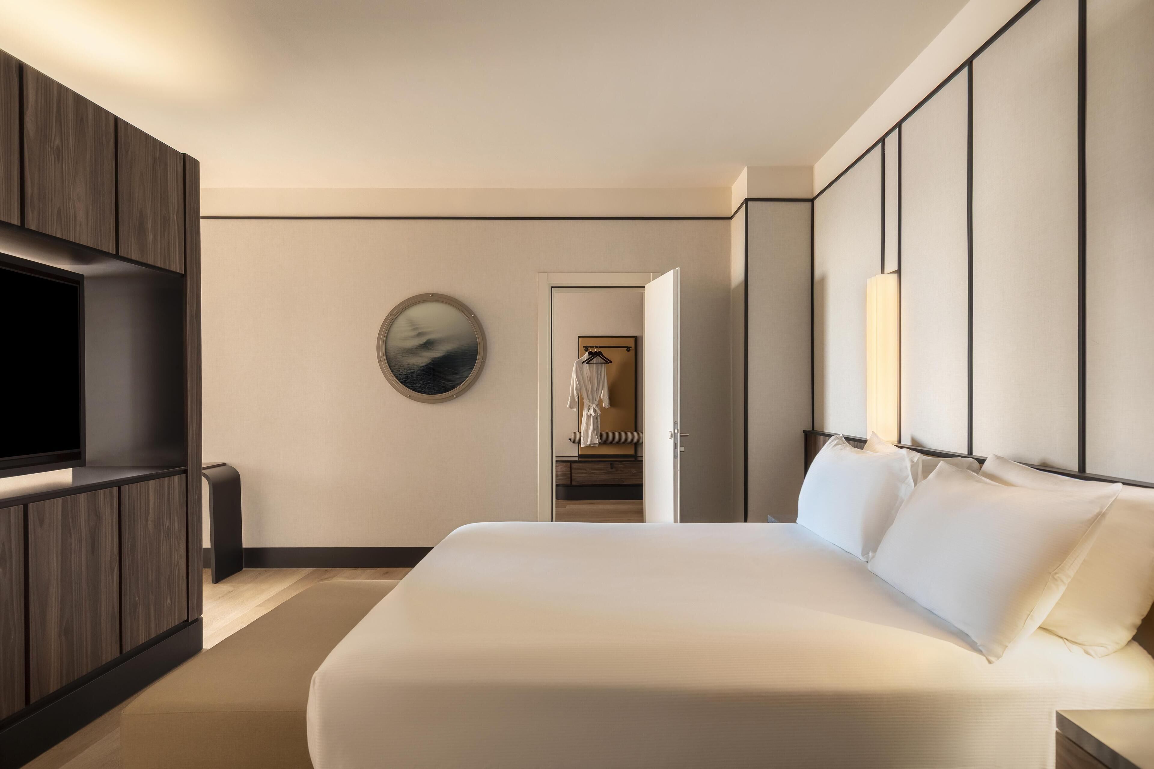Una habitación de hotel moderna con una cama grande, televisor y vestidor.