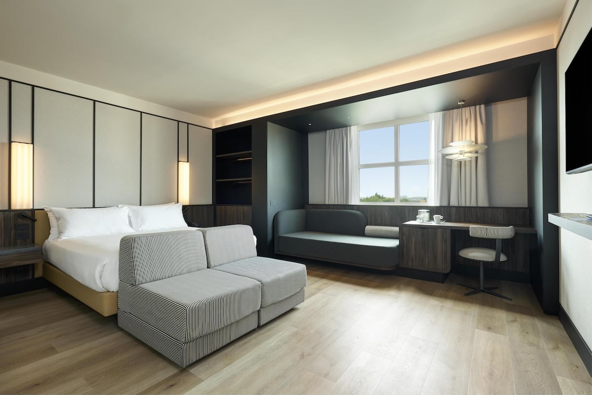 A modern hotel room with a bed, a sofa, a small table, and a TV.