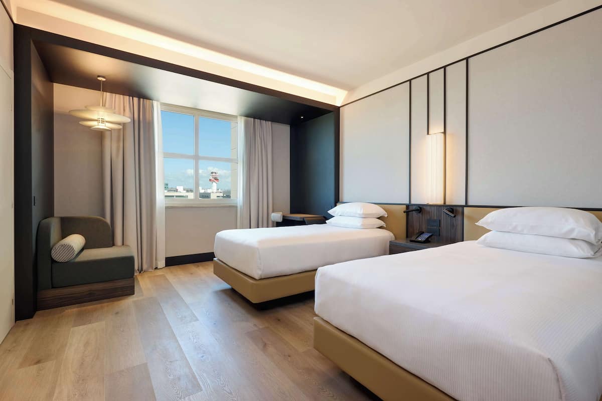 A hotel room with two beds, a sofa, a small table, and a window with curtains.