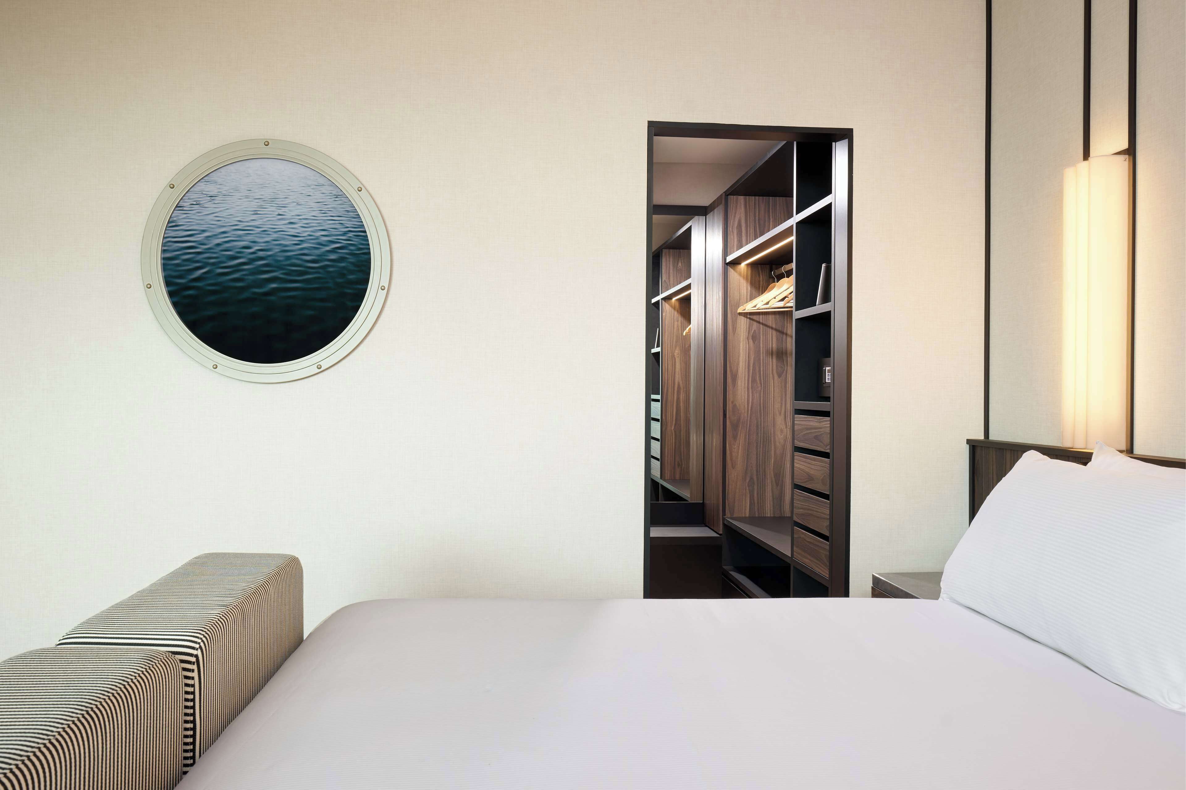 Ein Schlafzimmer mit einem Bett, einem runden Fenster mit Blick auf das Wasser, einem Kleiderschrank und einer Nachttischlampe.