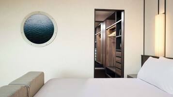 Ein Schlafzimmer mit einem Bett, einem runden Fenster mit Blick auf das Wasser, einem Kleiderschrank und einer Nachttischlampe.