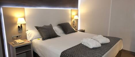 A hotel room with a large bed, two bedside lamps, a nightstand with a phone, and a chair.