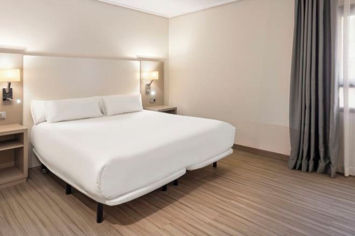 Une chambre d’hôtel avec un grand lit, des lampes de chevet, une table de nuit et une fenêtre avec des rideaux.