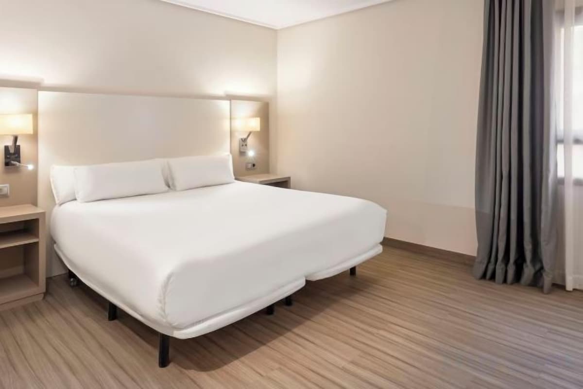 Ein Hotelzimmer mit einem großen Bett, Nachttischen und einem Vorhang am Fenster.