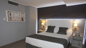 Ein Hotelzimmer mit einem großen Bett, zwei Nachttischen mit Lampen, einem an der Wand befestigten Kunstwerk und einer dunklen Decke.