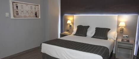 A hotel room with a large bed, two bedside tables with lamps, a wall-mounted artwork, and a dark ceiling.