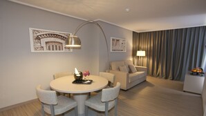 Ein modernes Hotelzimmer mit einem runden Esstisch, zwei Stühlen, einer Couch, einer Lampe und Kunstwerken an den Wänden.