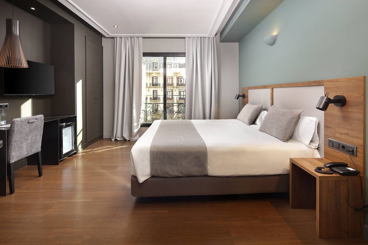Une chambre d’hôtel moderne avec un grand lit, un bureau et une vue sur les immeubles par la fenêtre.
