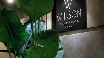A sign for the Wilson Boutique Hotel with large green leaves in the foreground.