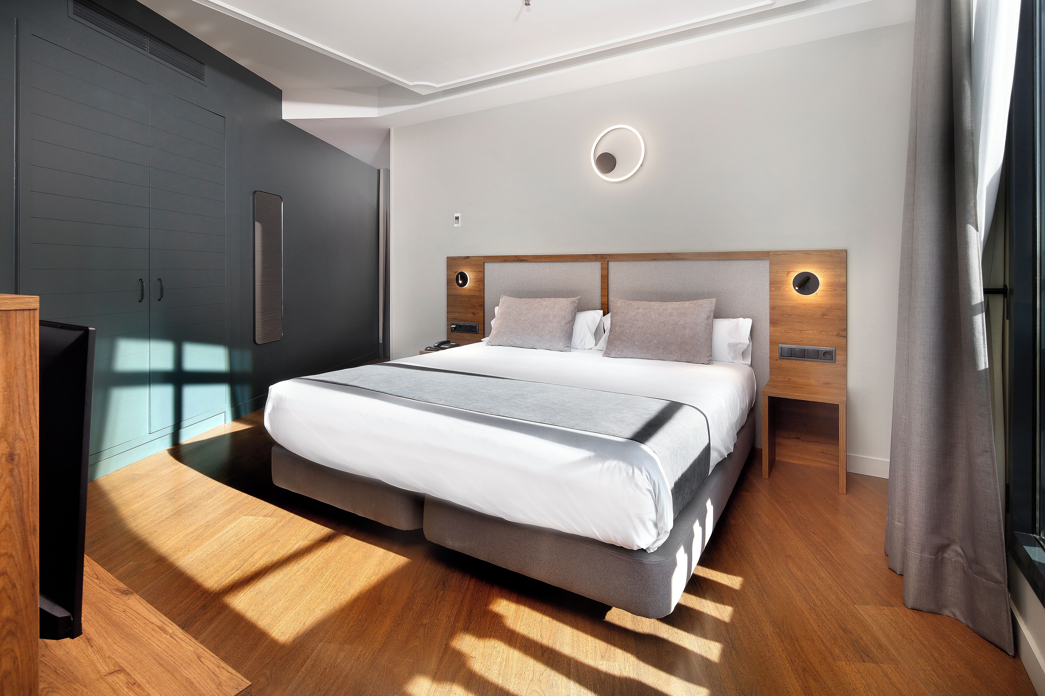 A modern bedroom with a large bed, wooden flooring, built-in wardrobe, and bedside lamps.