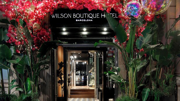Entrada do Wilson Boutique Hotel em Barcelona, com flores vermelhas iluminadas e grandes esferas decorativas.