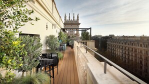 Terraço no telhado com deck de madeira, área de estar ao ar livre e vista para um edifício histórico.