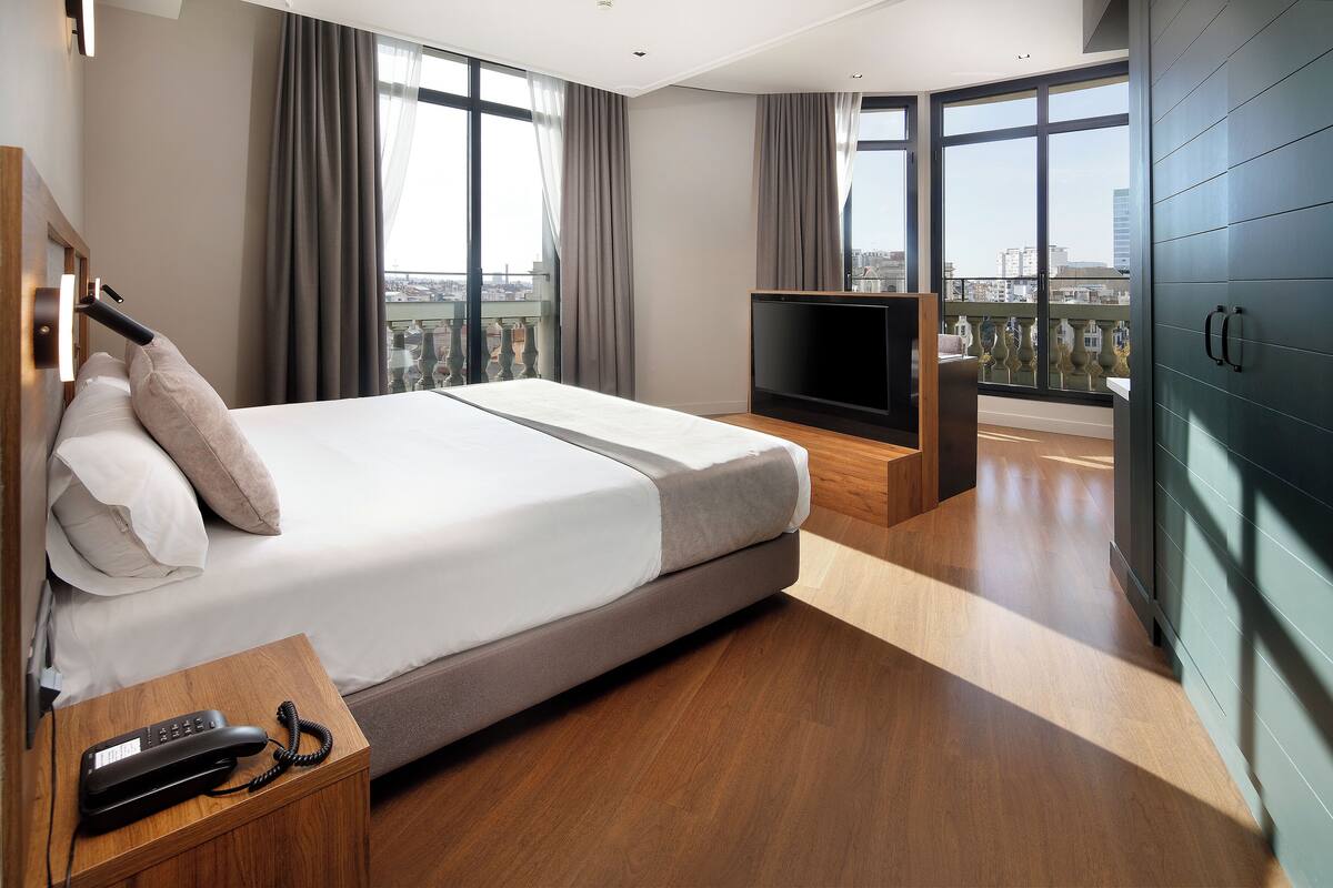 Une chambre d’hôtel moderne dotée d’un grand lit, d’une télévision et d’un balcon offrant une vue sur la ville.