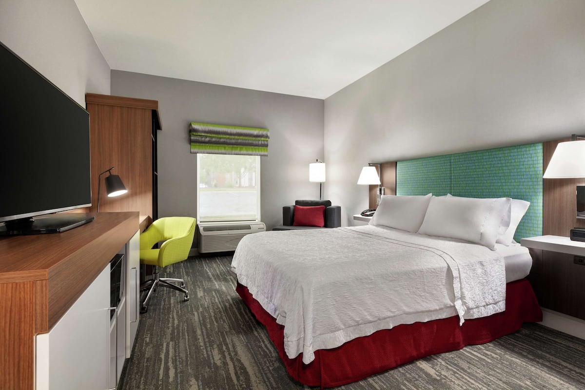 Habitación de hotel con cama, escritorio, televisor, silla y ventana con vistas.