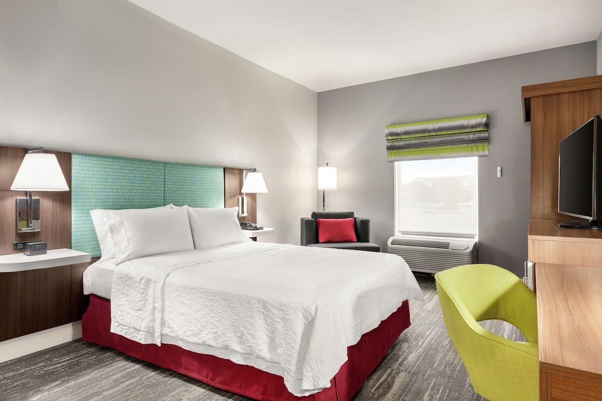 Habitación de hotel con cama, escritorio, silla, televisor y ventana con vista.