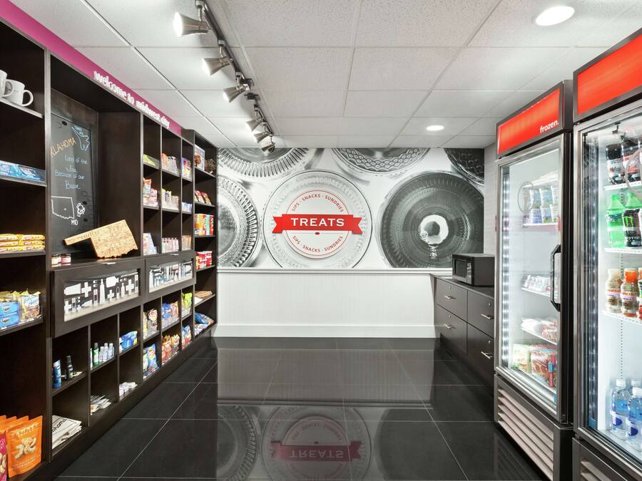 A clean, modern snack bar with shelves stocked with various snacks and beverages, a chalkboard sign, and a refrigerator.