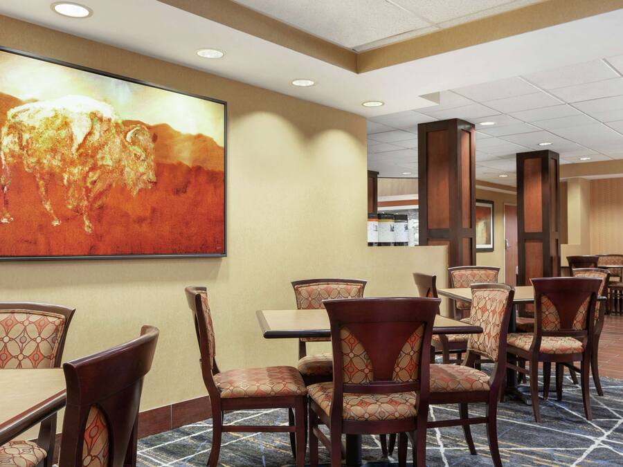 Un comedor de hotel con mesas y sillas, un cuadro grande en la pared y suelo de baldosas.