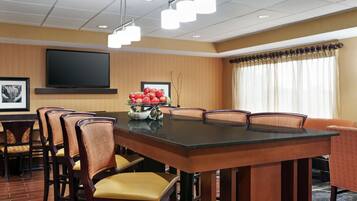 A conference room with a large table, chairs, a flat-screen TV, and a fruit bowl.