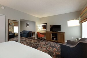 Habitación de hotel con cama, escritorio, televisor, silla y piso alfombrado.