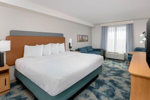 A hotel room with a large bed, a desk, a chair, a sofa, a painting on the wall, and a window with curtains. - Hampton Inn & Suites Austin-Airport (Austin)