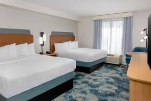 A hotel room with two beds, a desk, a chair, a lamp, and a window with curtains.