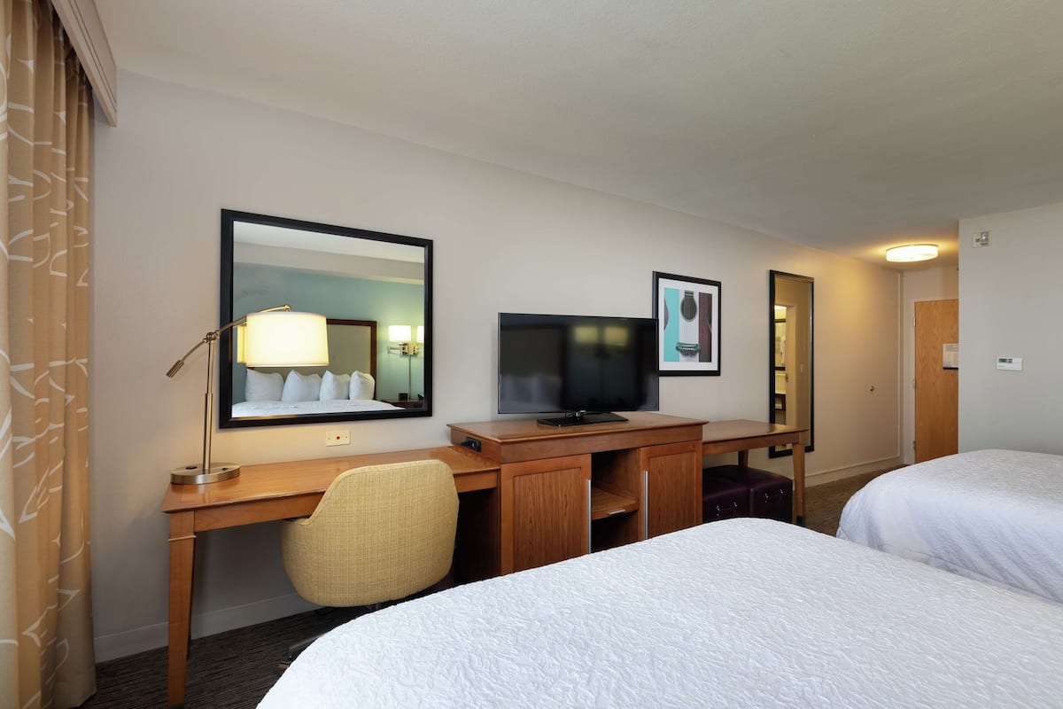 A hotel room with two beds, a desk with a television, a chair, and a large mirror.