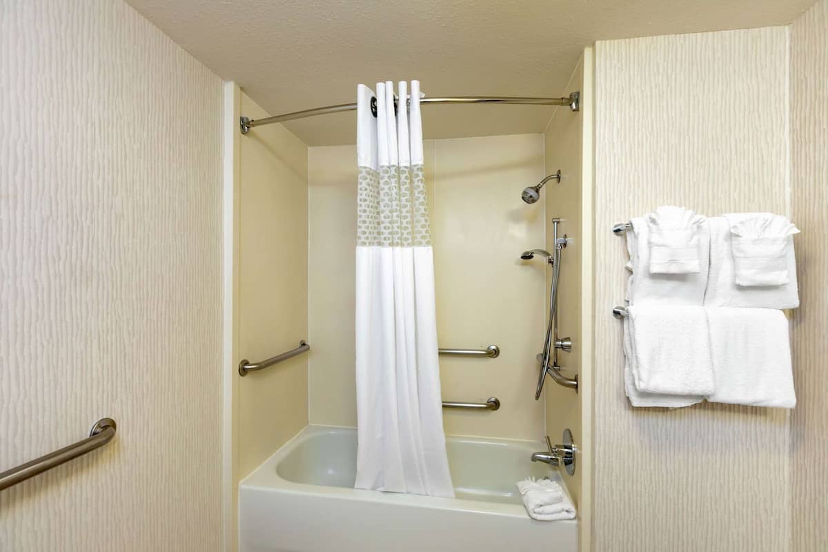 A bathroom with a bathtub, shower, and handrails.