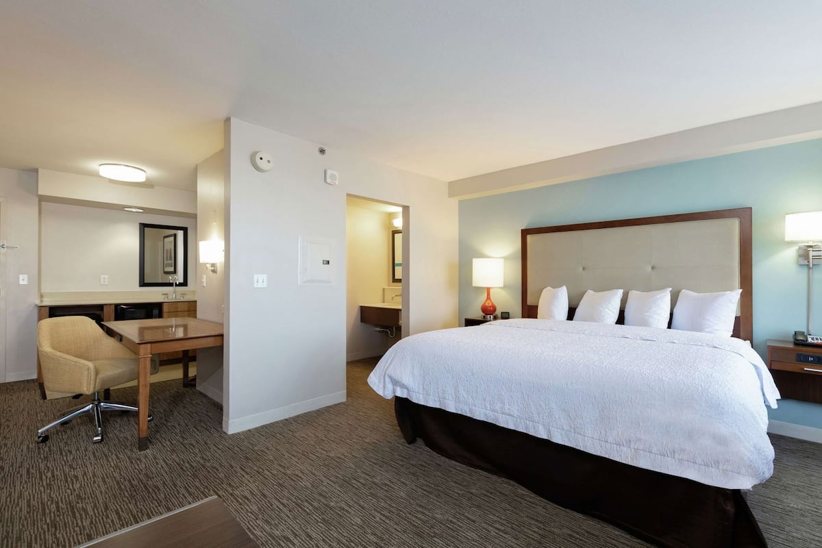 A hotel room with a bed, a desk, a chair, a nightstand, and a lamp.