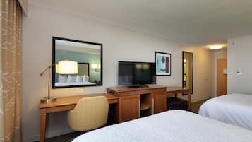 A hotel room with a desk, a television, two beds, and a mirror.